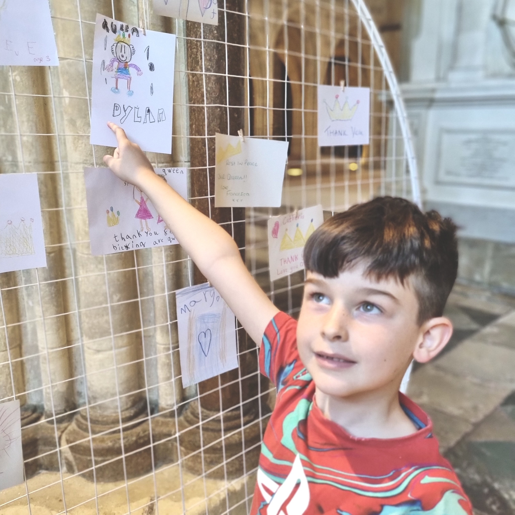 A child points to their drawing for Her Late Majesty Queen Elizabeth II