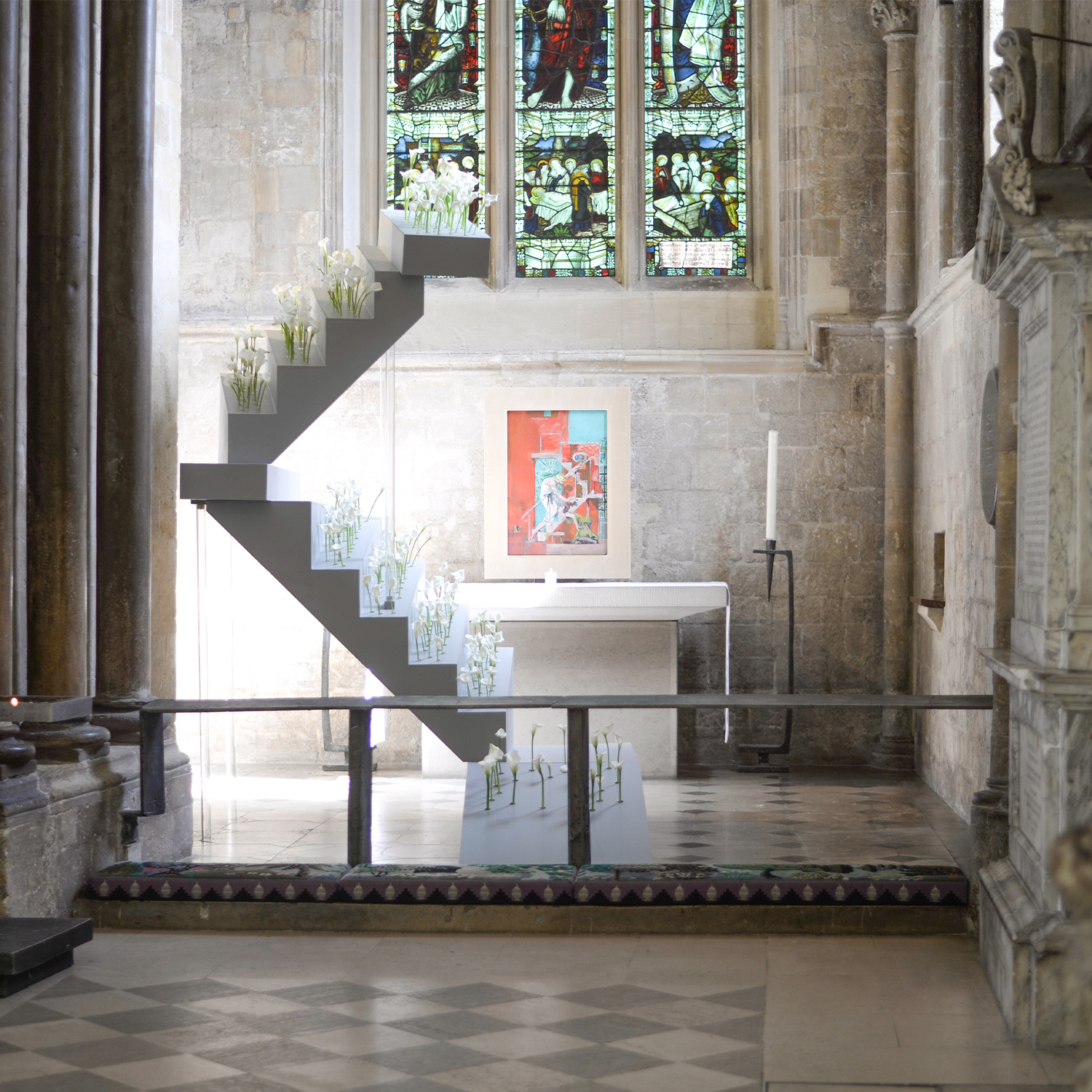 A floral installation, in the shape of a grey staircase, with single stems of white lilies in individual tubes.