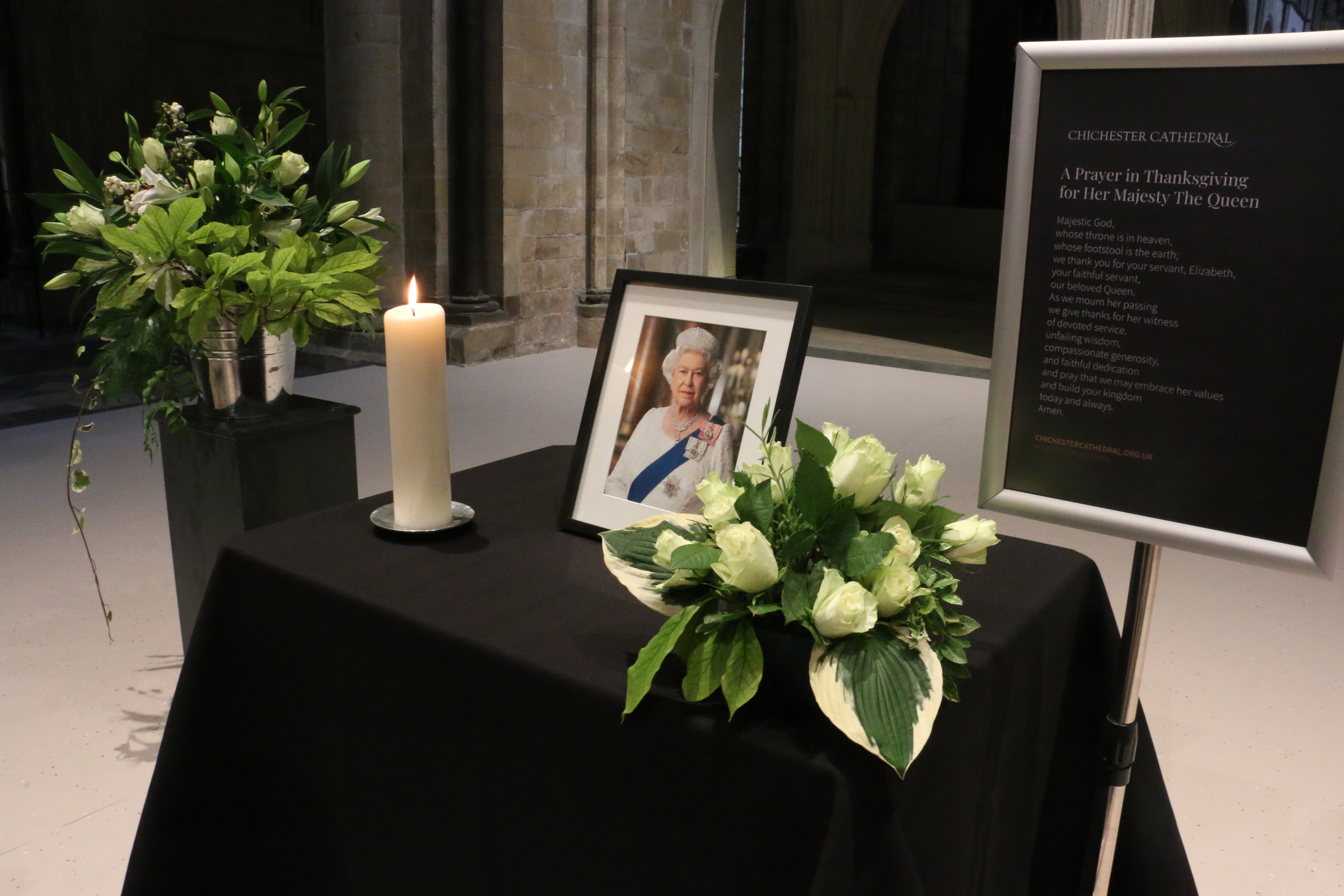 A photograph of Her Late Majesty Queen Elizabeth II with a candle and flowers