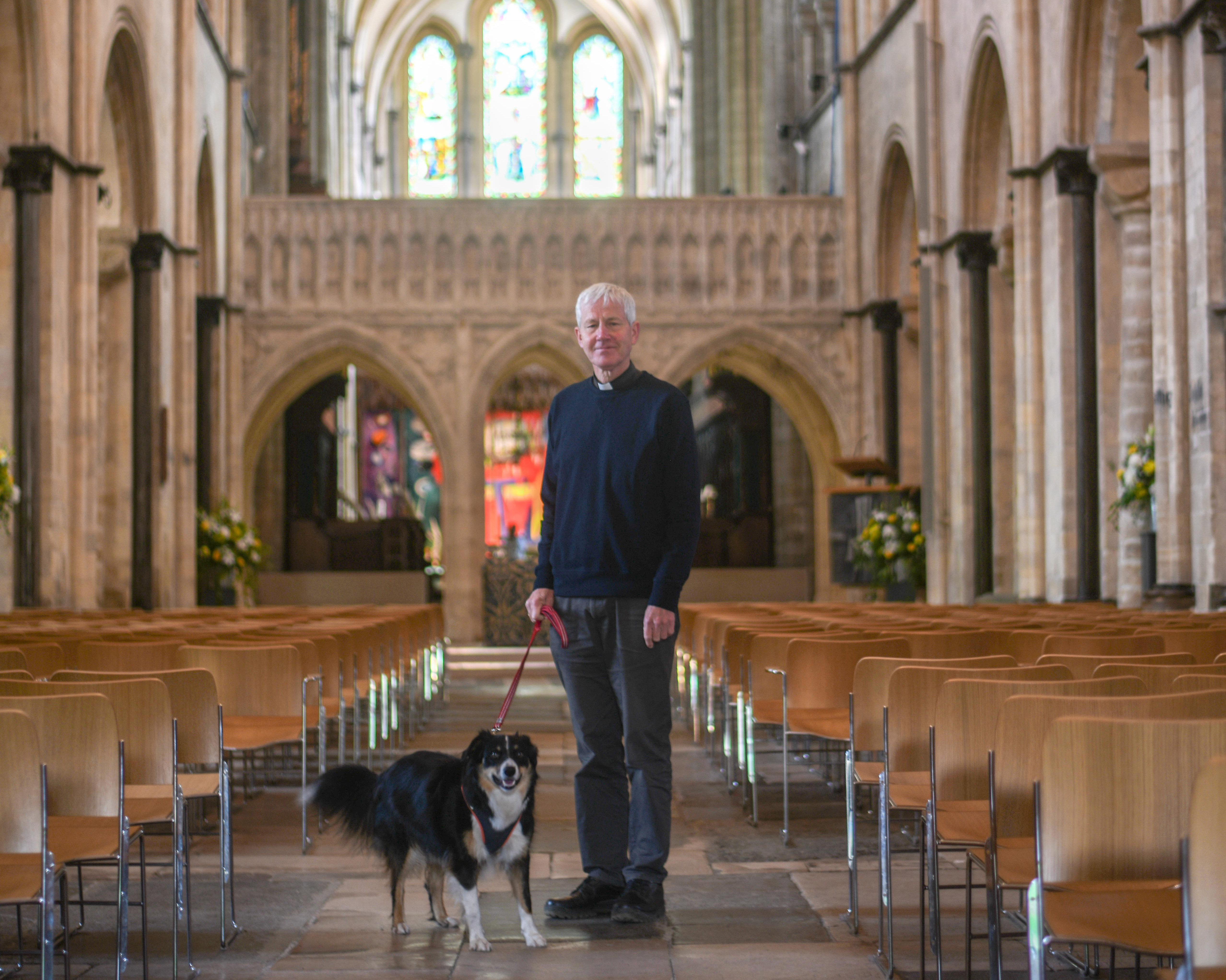 Interim Dean of Chichester, The Reverend Canon Simon Holland stands in the Cathedral Nave with his dog, a brown, black and white English Shephard