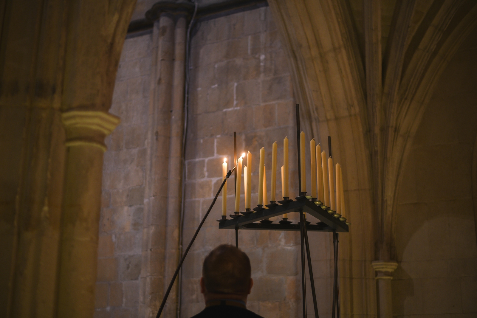 A Verger lights tall candles using a long taper