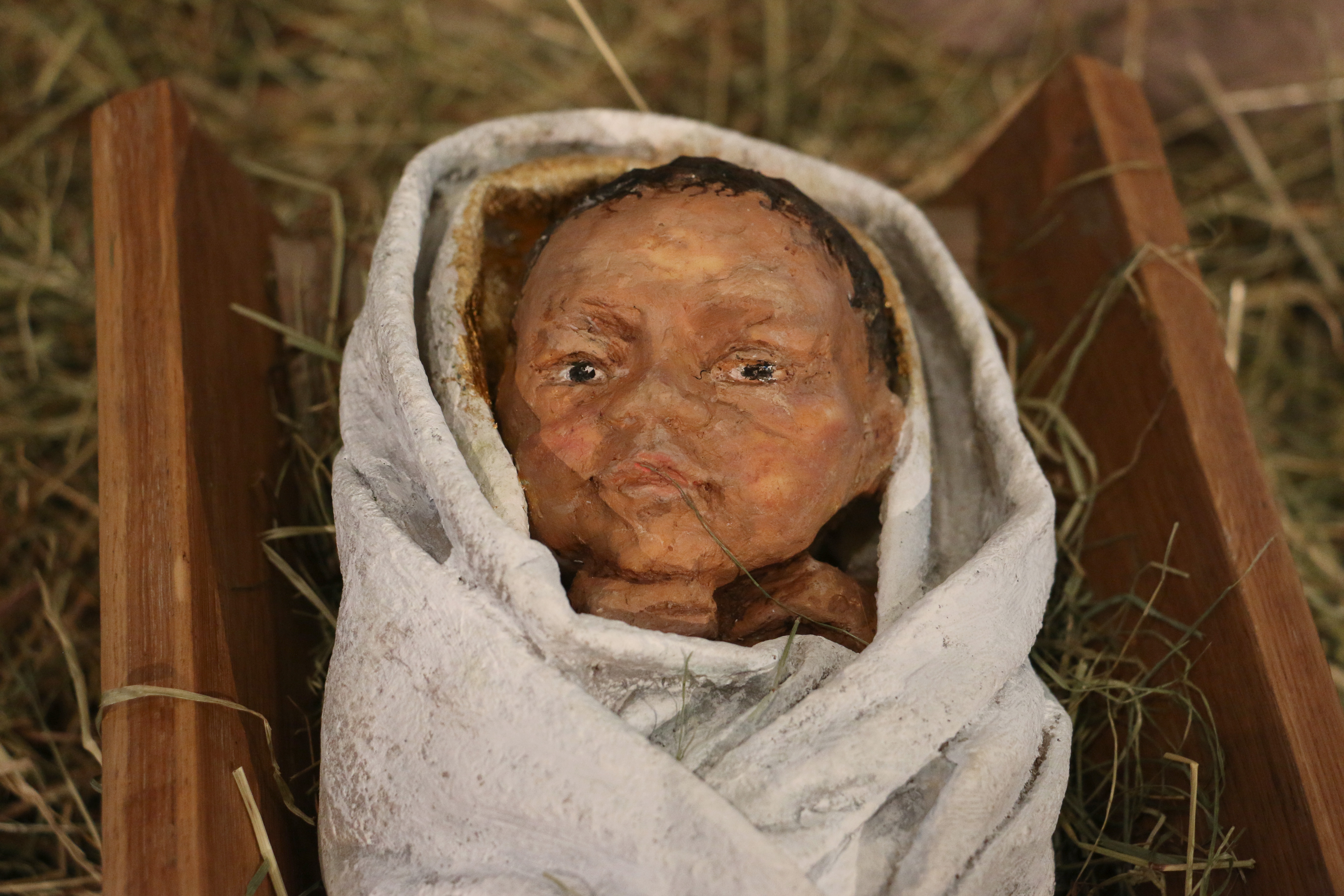 Close up of the Christ child face swaddled in white cloth, with the hands resting below the chin
