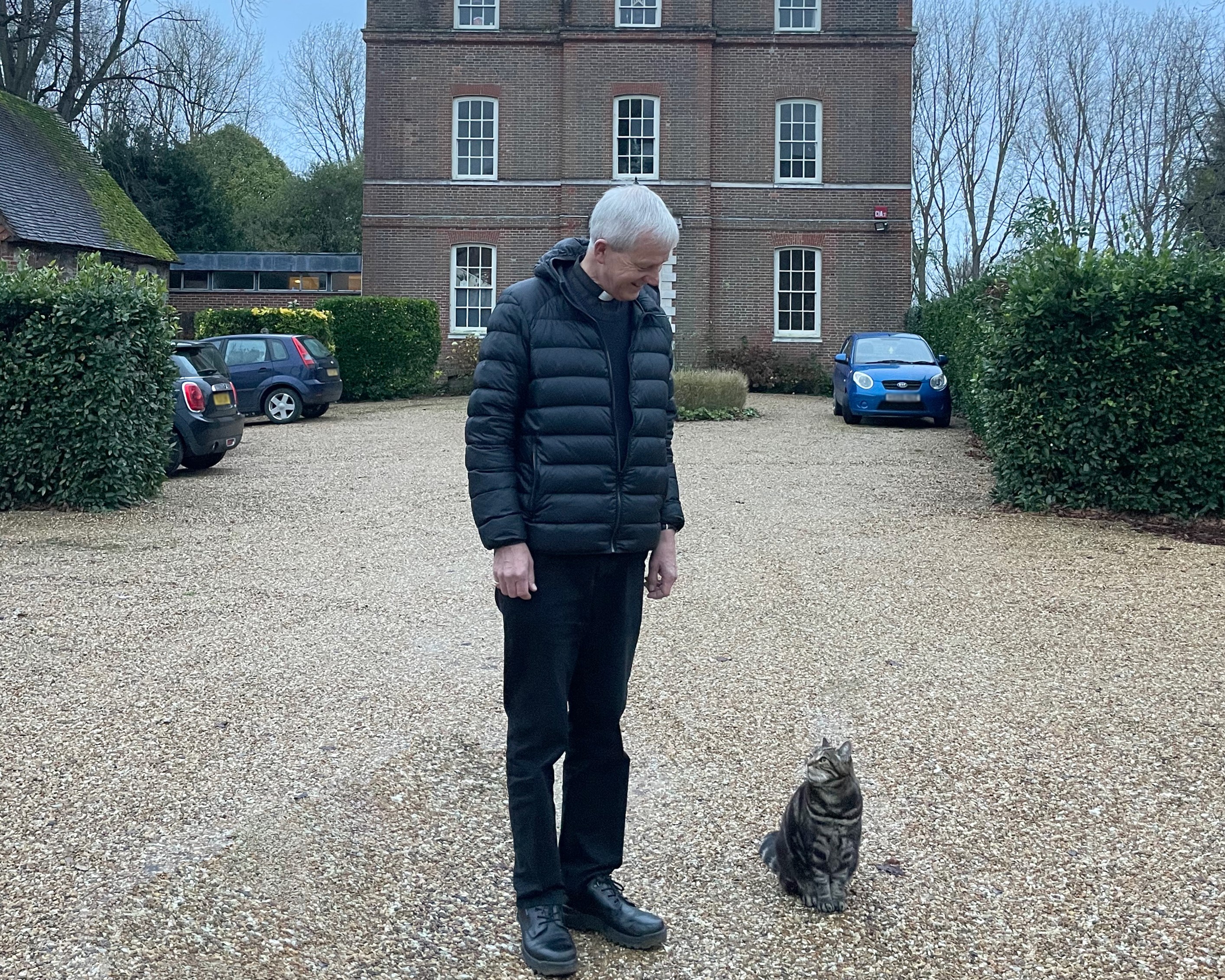 Interim Dean of Chichester, The Reverend Canon Simon Holland stands in front of the Deanery with Bertie, a tabby brown cat