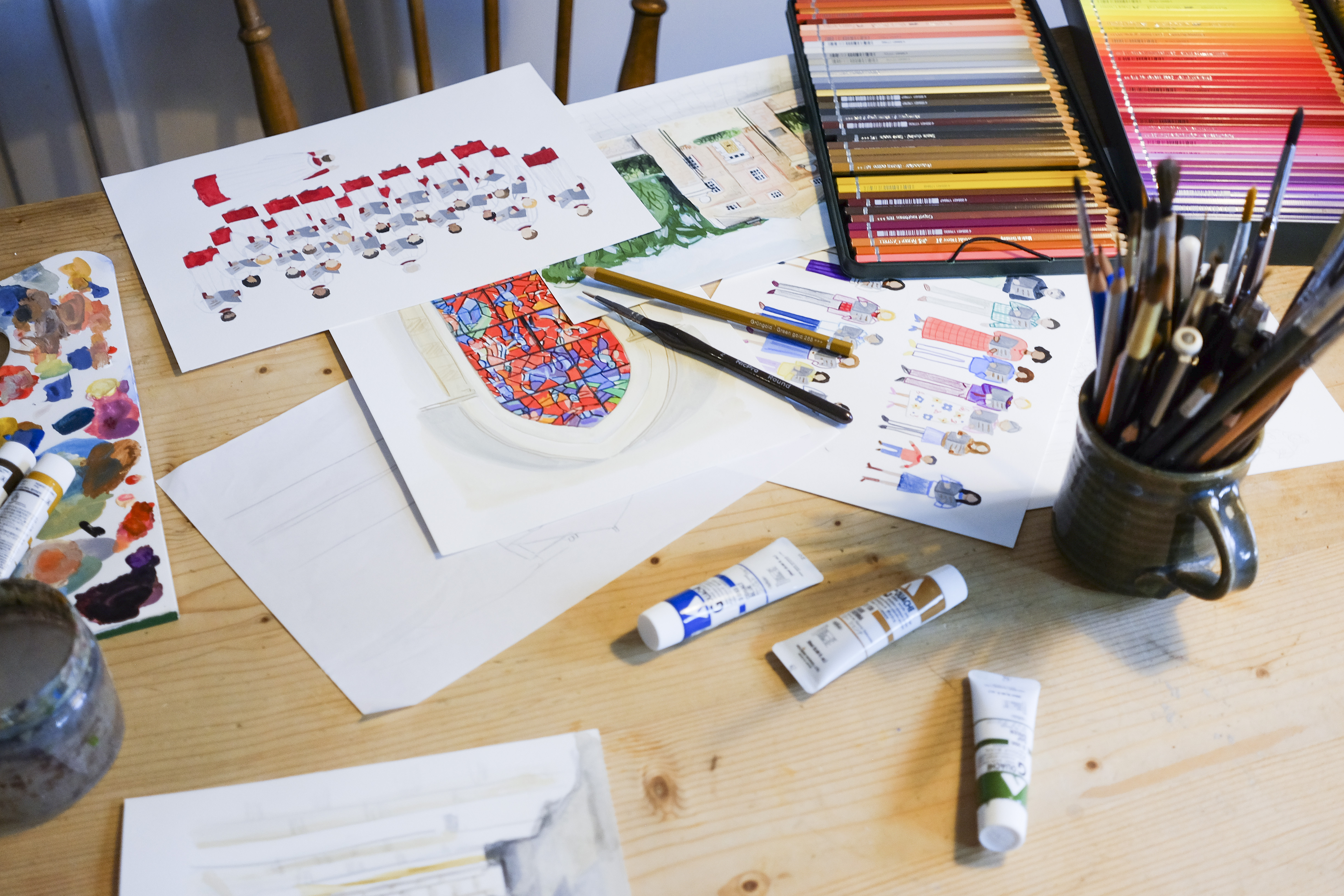 A table with paints, paintbrushes, pencils and paper with illustrations from Bertie the Cathedral Cat's story