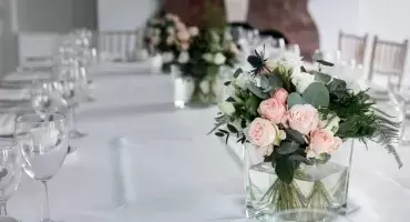 Light pink wedding flowers in a vase sit on a table with white cloth