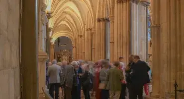 A large group of people congregating in the Cathedral, with grey stone arches framing the photograph
