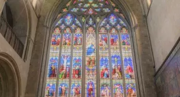 A large stained-glass window reflecting different biblical stories, with strong blue and red coloured glass