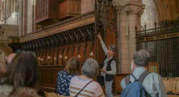 A volunteer speaking to a tour group and points at the Cathedral organ which has dark wooden and gold decorated pipes