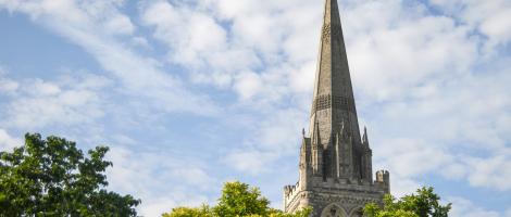 The spire of the Cathedral behind full green trees