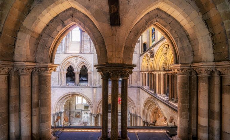 View from within Chichester Cathedral's Triforium level, looking through stone arches towards the nave below and upper gallery beyond.