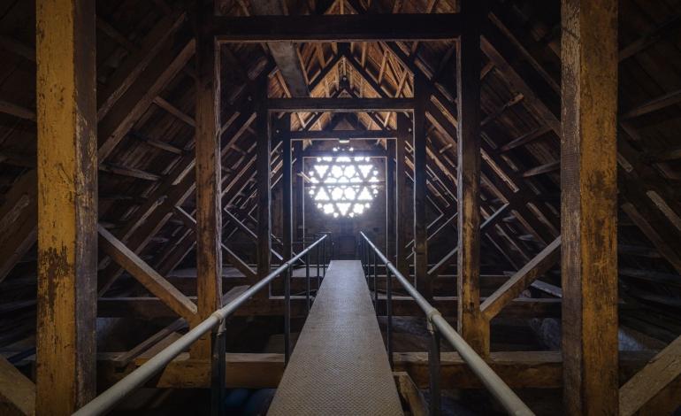 Walkway through the medieval timber roof structure of Chichester Cathedral, leading towards a circular window.
