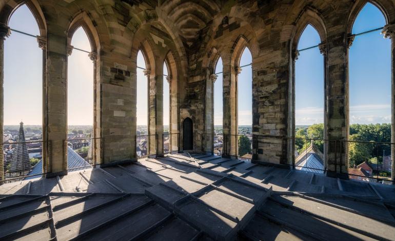 View of Chichester Cathedral's bell tower and roof from above, with the city of Chichester and surrounding countryside beyond.