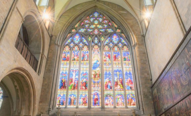 The vibrant east transept window fills the Cathedral with coloured light, showcasing intricate stained glass beneath soaring Gothic arches and stone tracery.
