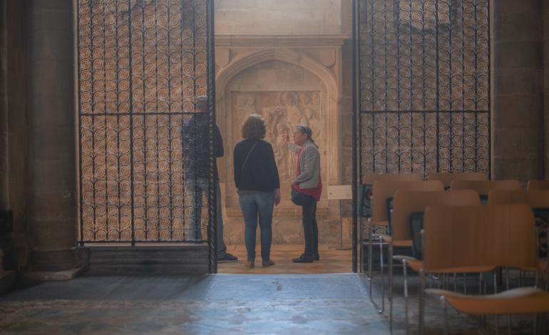 A guide shows two visitors one of the Chichester Reliefs, a medieval stone carving