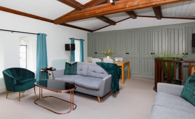 Wooden doors behind a dining table adjacent to the grey sofas, as a dining/living area joined