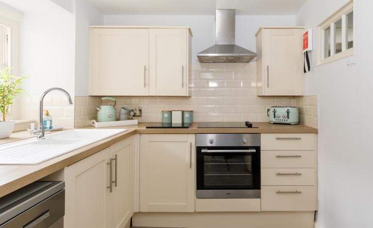 Fully equipped kitchen with cream cupboard, sink, toaster, dishwasher, kettle and coffee machine, oven, hob and extractor hood