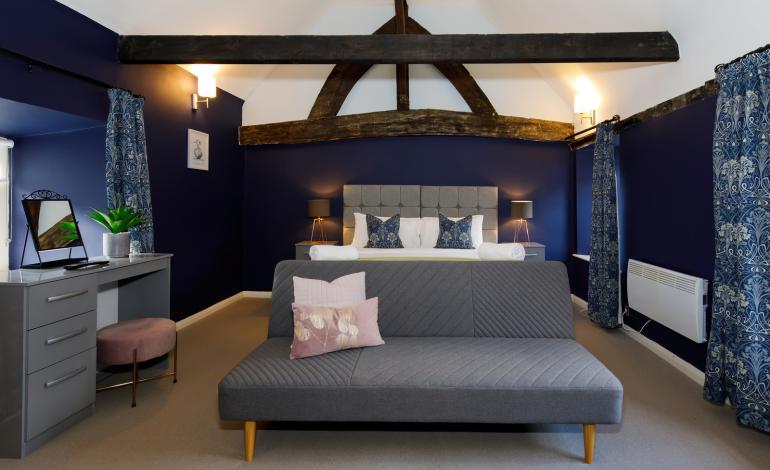 Larger bedroom with exposed beams in the ceiling. Large double bed which can be 2 singles, with small sofa at the end of the bed which becomes a sofa bed, bed side table, dresser and chair with mirror