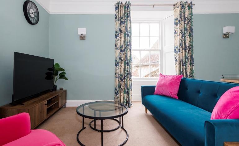 Sitting room with blue sofa and pink armchair with television.