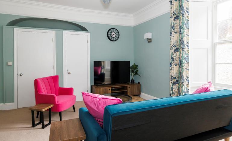 Living room view with sofa, pink armchair and television.