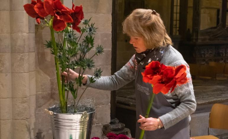 A woman  places red flowers in a floral display bucket