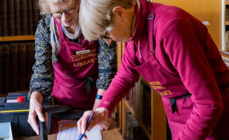 Two cathedral librarians covering an old book to help preserve it