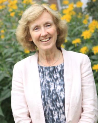 Prof Jane Longmore stands in front of yellow flowers