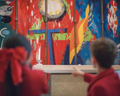 Two children in red school uniforms standing near the High Altar at Chichester Cathedral, looking toward John Piper’s colourful High Altar Tapestry behind the altar.