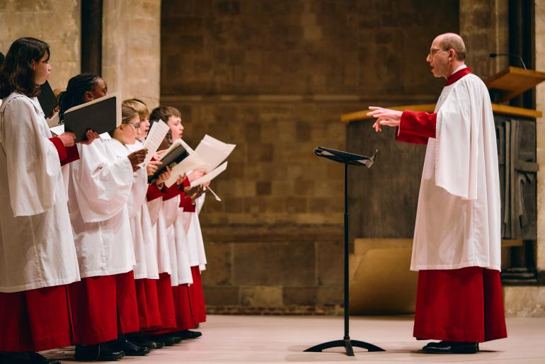 Charles Harrison conducts Cathedral Choristers. All wear red and white cassocks.