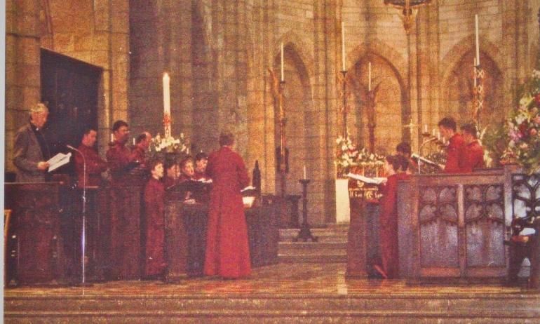 A choir in red robes are rehearsing in a cathedral