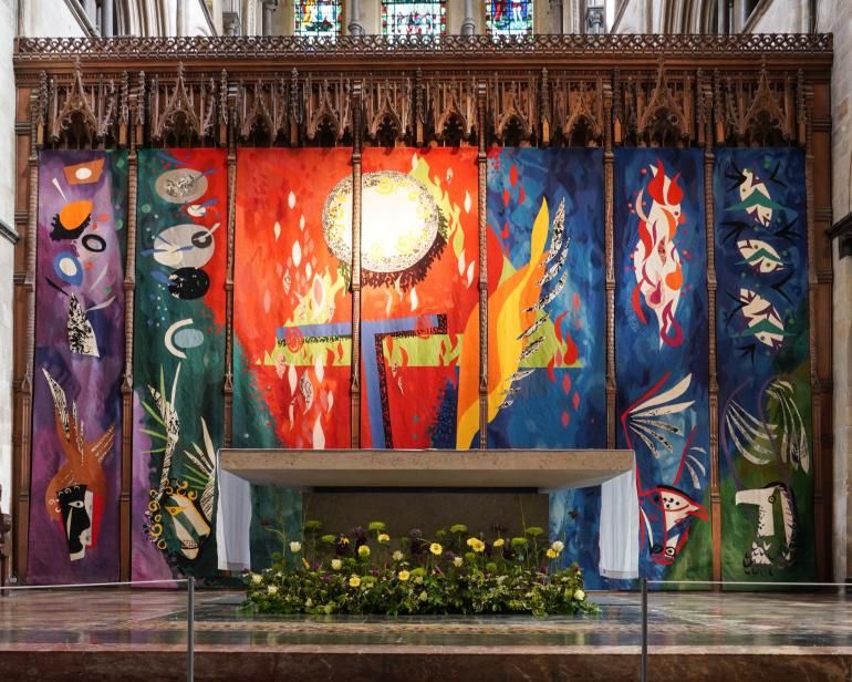 A full, unobstructed view of John Piper’s High Altar Tapestry behind the High Altar at Chichester Cathedral, showing its large abstract panels in vivid colours including red, blue, green and yellow.